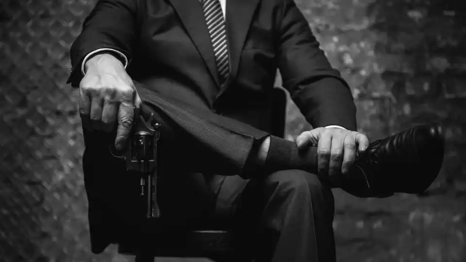 Seated man in a suit holding a pistol.